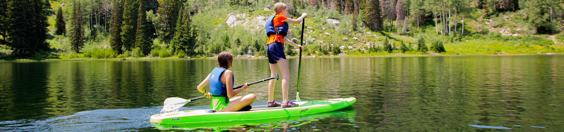  two girl scouts on a paddle board in a lake 