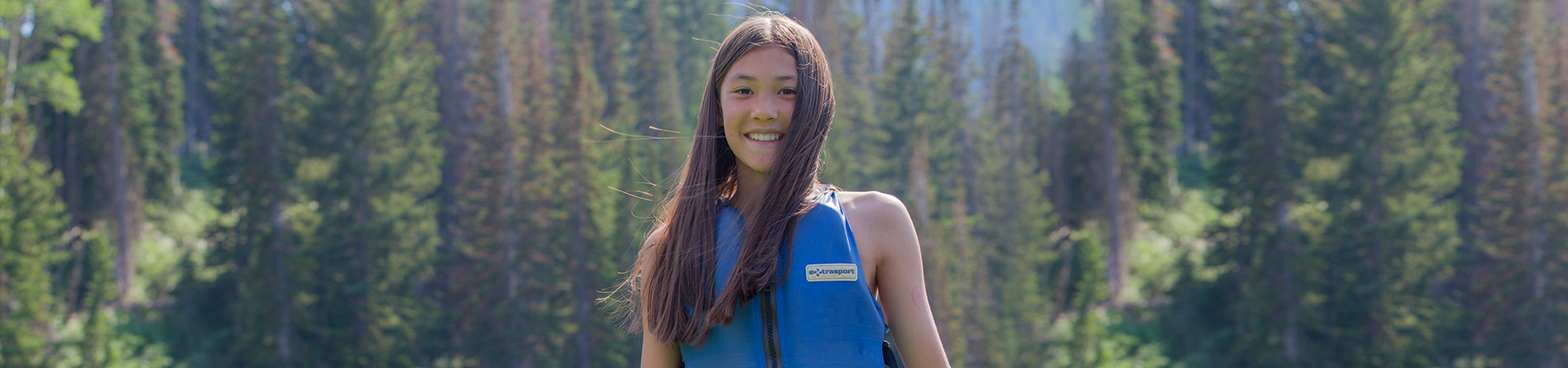  girl scout wearing life vest stands in front of a forest 