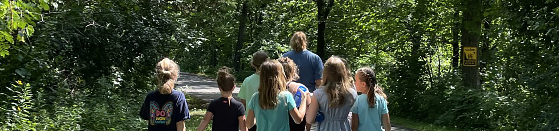  group of girl scouts hike on a trail through the woods 