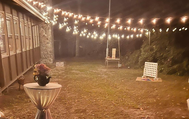 outside of dining hall set up for a wedding with twinkle lights, decorated cocktail tables and lawn games