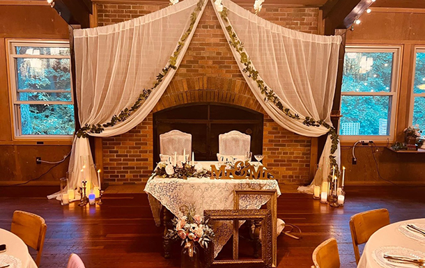 decorated sweetheart table in front of fireplace and decorate backdrop in the dining hall for a wedding