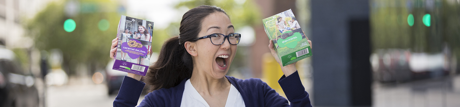  adult girl scout volunteer excitedly holding two girl scout cookie boxes 