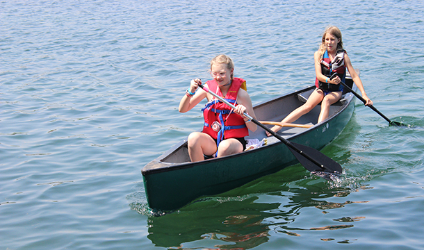 two middle school age girls paddle boarding on a lake