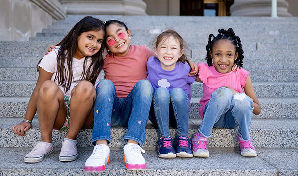 four elementary-school-age girls sit on steps outdoors