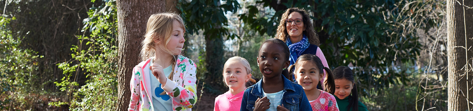  group of younger girl scouts hiking through woods with adult leader behind them 