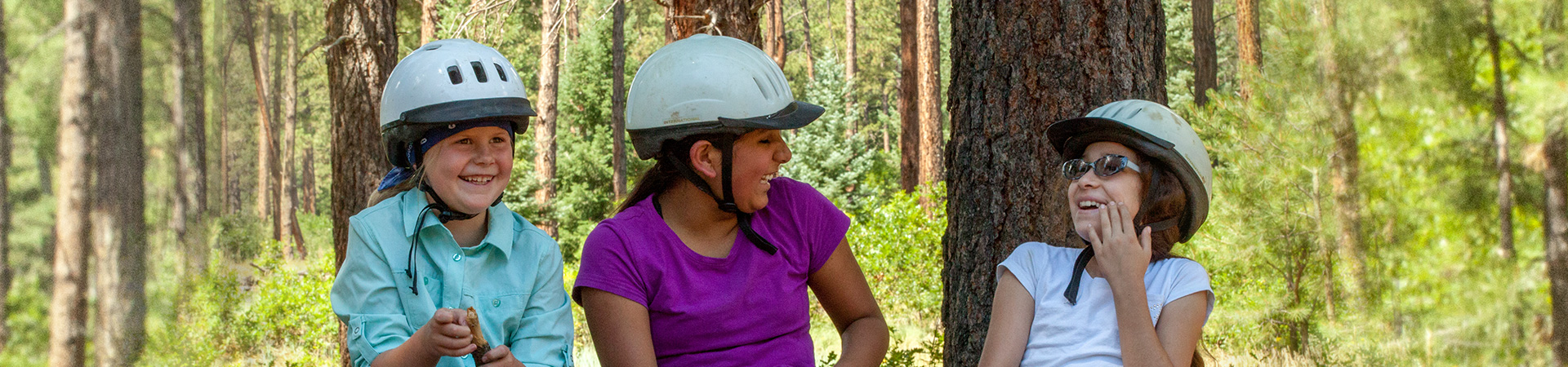  two girl scouts and an adult wearing helmets and laughing 