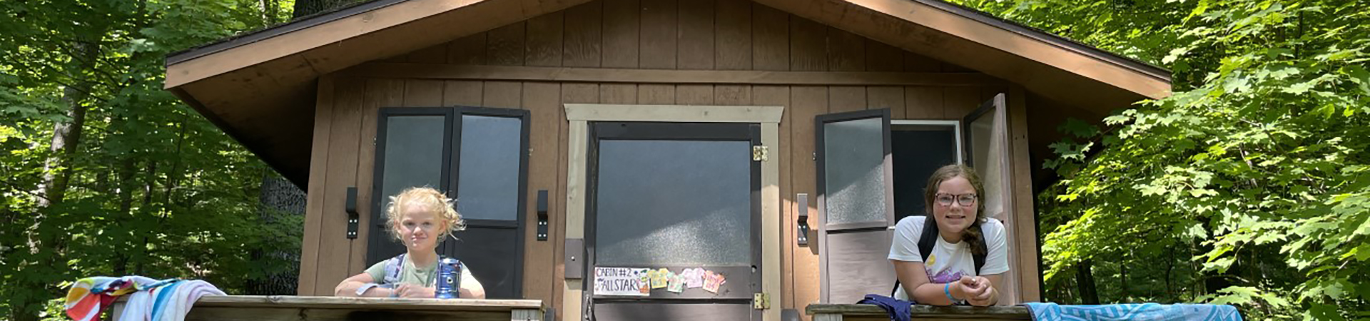  two girl scouts pose outside of a cabin at camp 