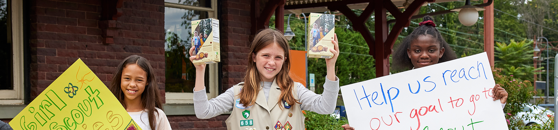  group of girl scouts hold cookie boxes and signs at a cookie booth 