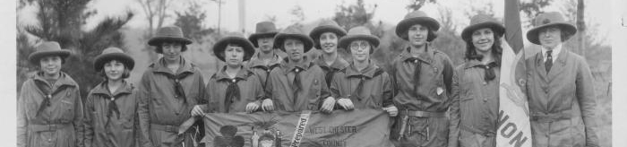  historic black and white photo of a group of girl scouts standing outside holding a banner and flags 