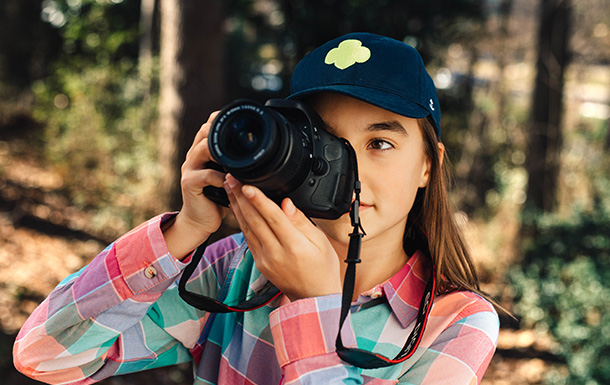 preteen girl scout taking a hiking holding a camera 