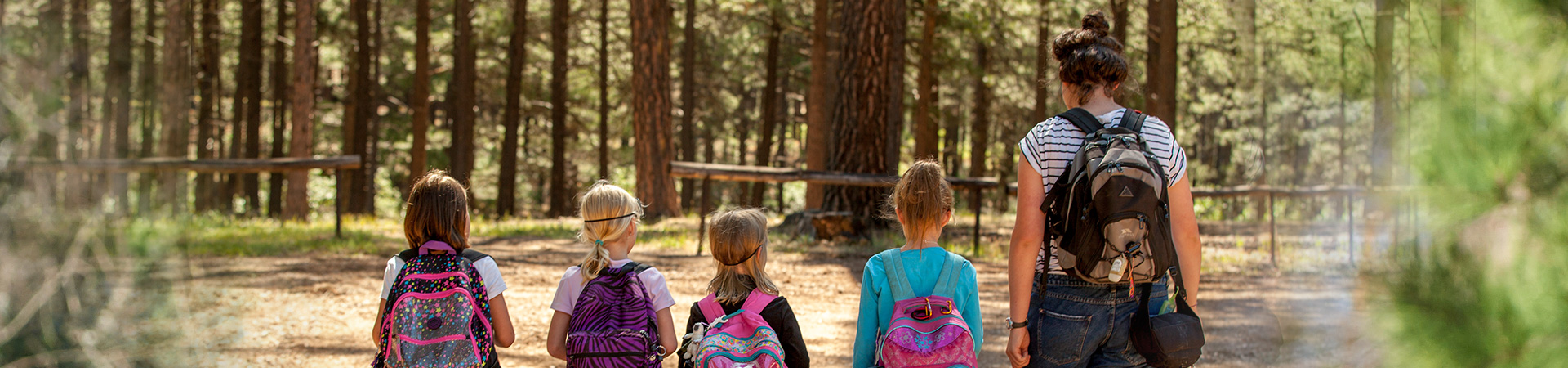  group of young girl scouts with an older adult volunteer hiking through woods 